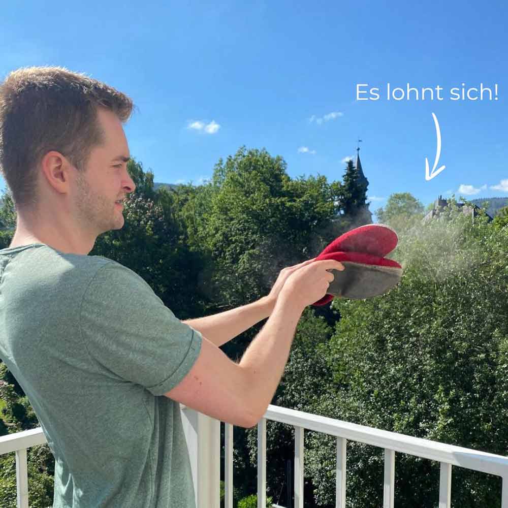 WoolFit Chef Benni klopft seine Pantoffeln im Freien aus und es entsteht eine große Staubwolke. Pantoffeln ab und zu ausklopfen, lohnt sich.